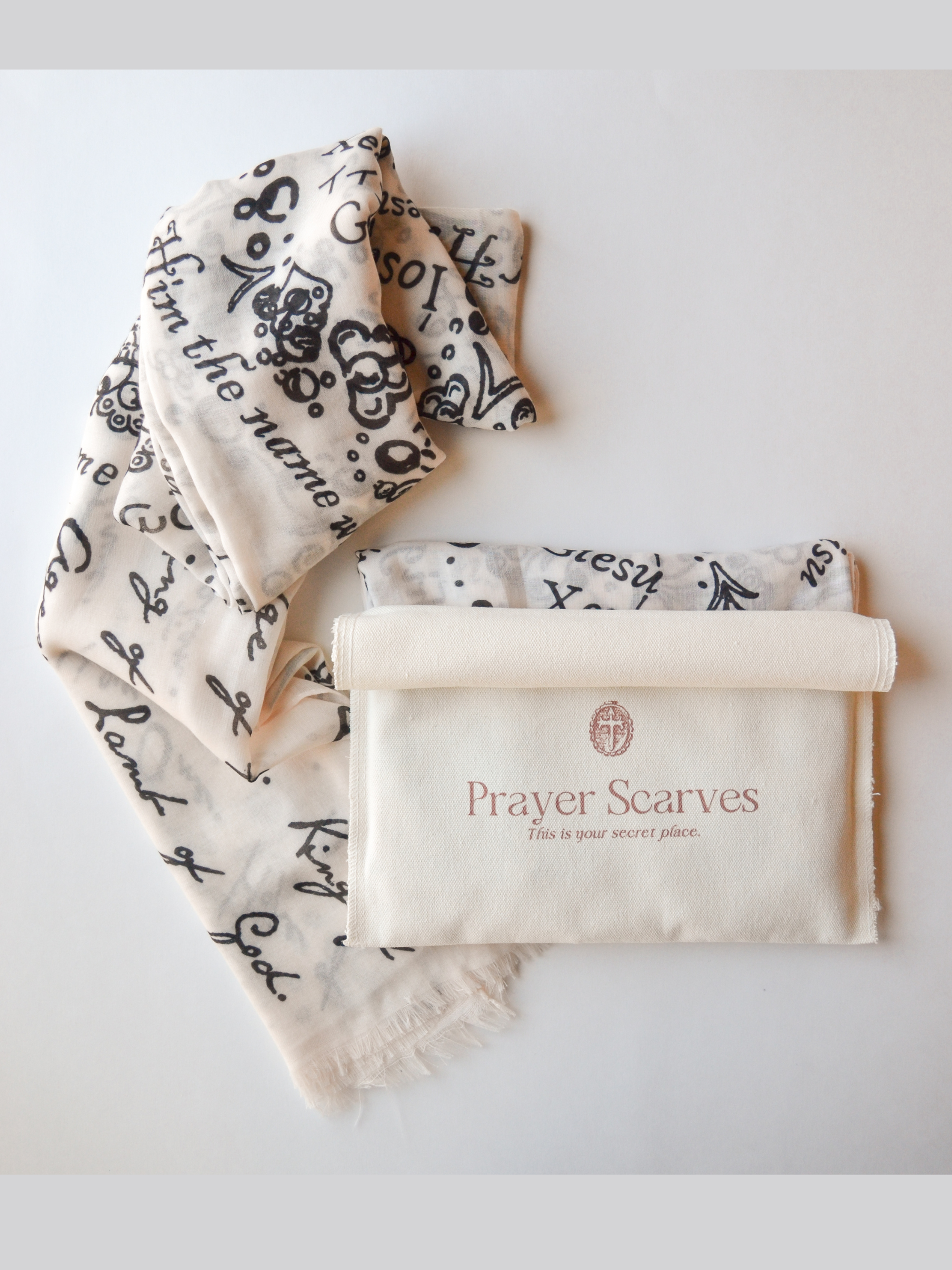 And He Shall Be Called prayer scarf by Prayer Scarves® folded on a light surface beside the branded storage pouch, highlighting the soft, lightweight fabric and handwritten names and titles of Jesus