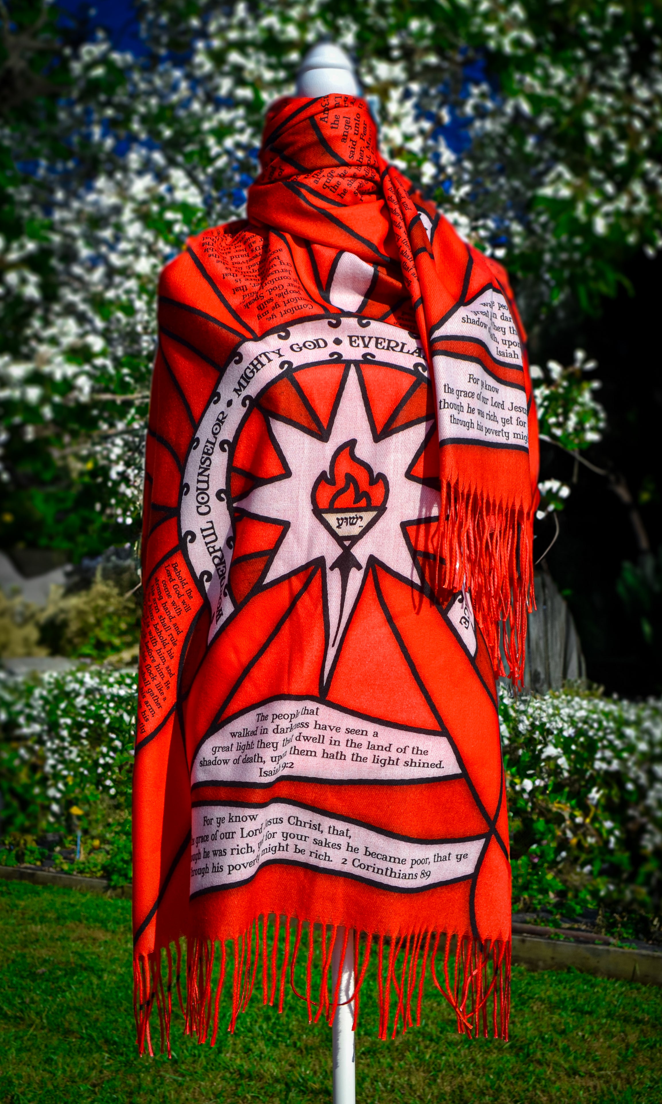 Red Advent Prayer Scarf by Prayer Scarves® displayed on a mannequin outdoors, showing bold red stained-glass–style panels, black lead-style outlines, and printed scripture text along the design.