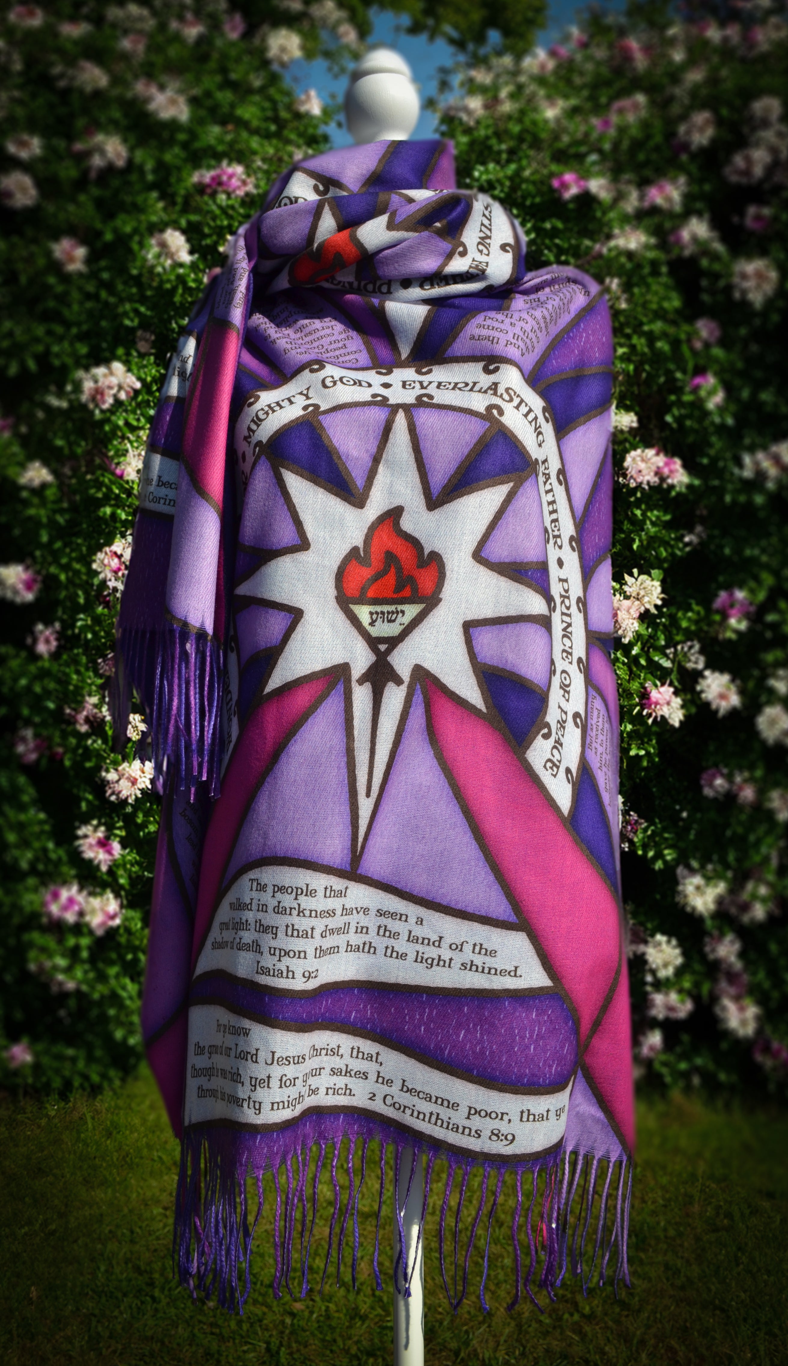 Purple Advent Prayer Scarf by Prayer Scarves® shown draped on a mannequin outdoors, highlighting stained-glass–style purple and pink sections, black lead-style lines, a central flame design, and printed scripture elements.