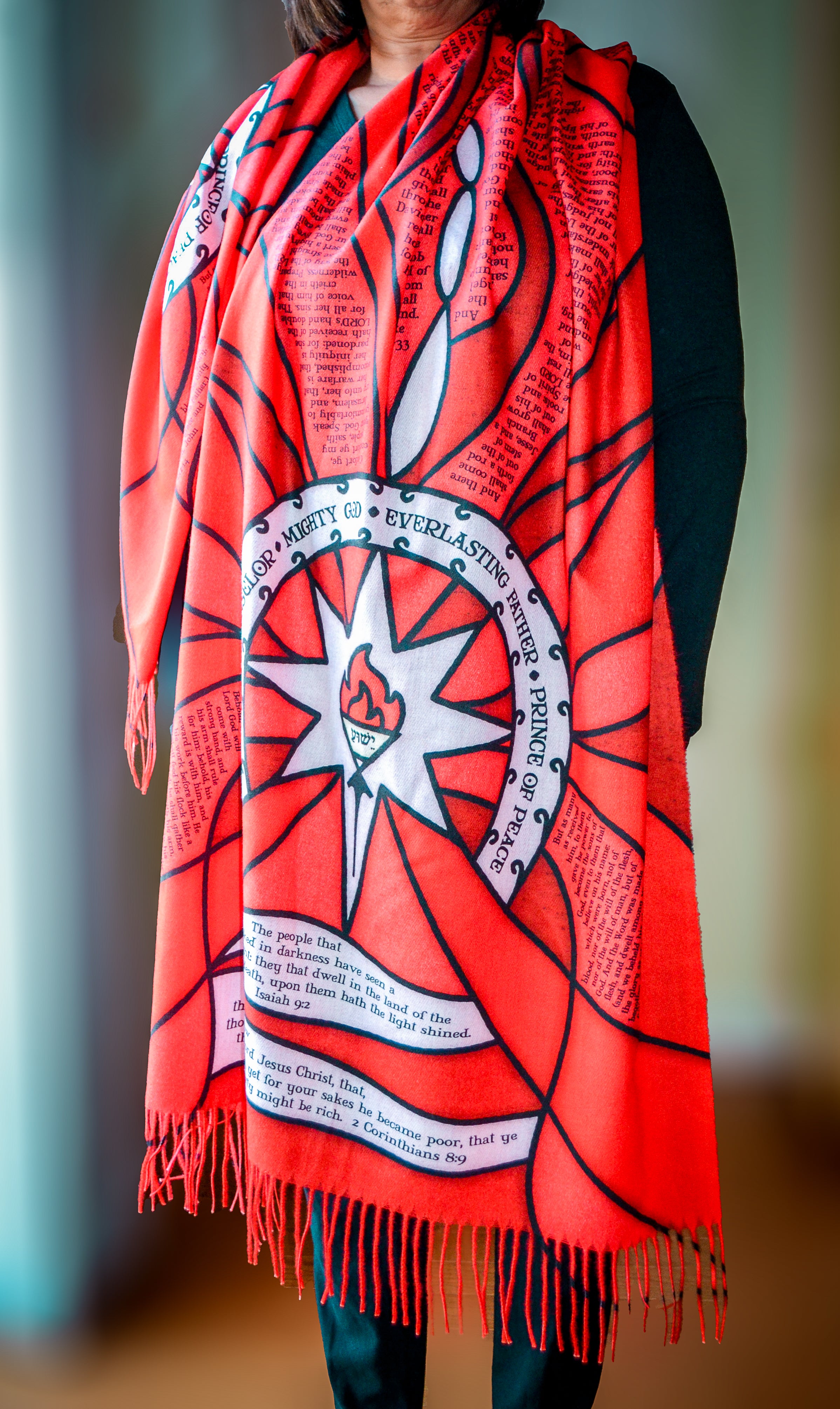 Model wearing the Advent Prayer Scarf™ in red tones, featuring a stained-glass–inspired design with scripture text woven throughout.