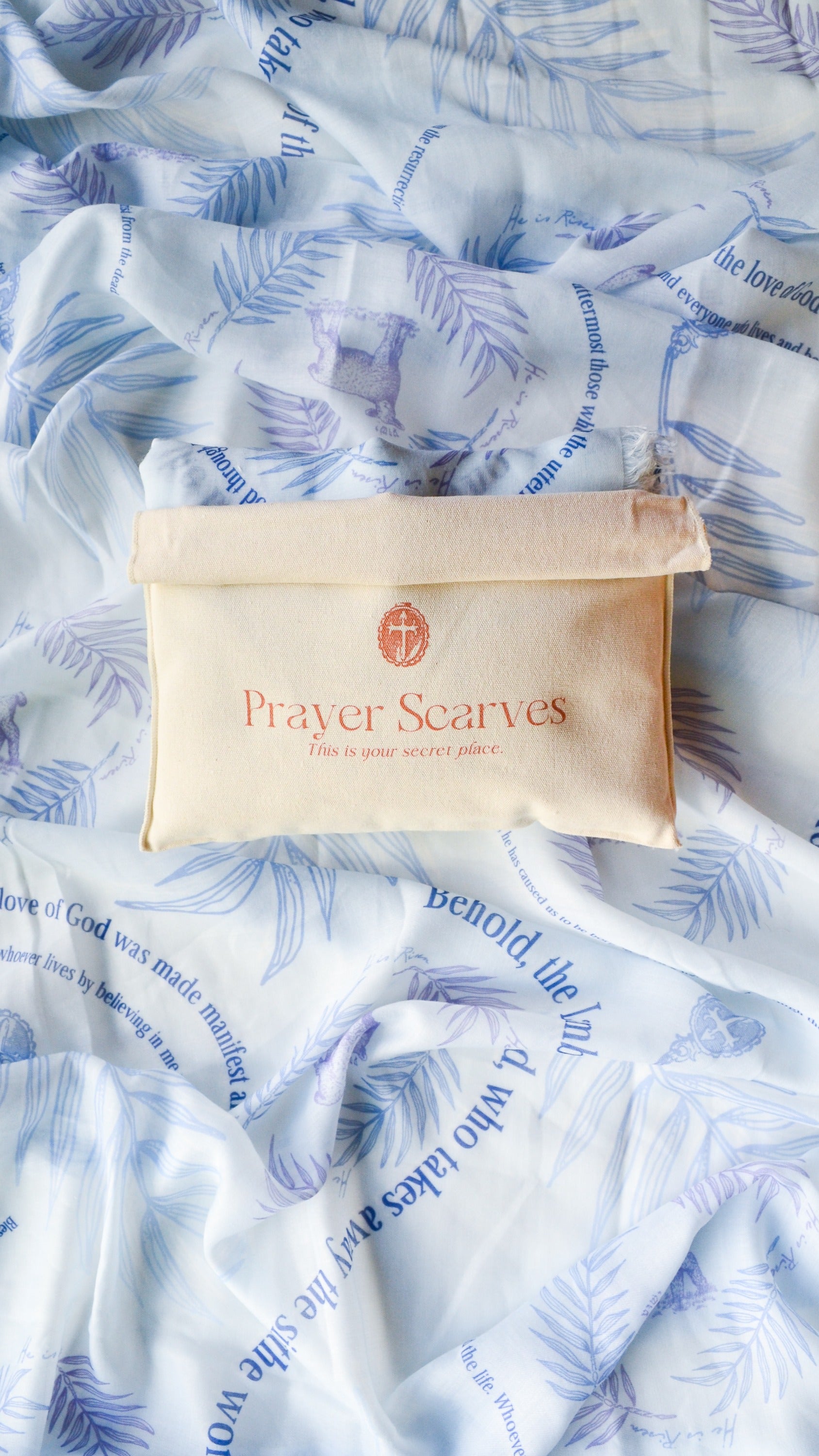 Light blue Hosanna prayer scarf featuring palm branch and lamb illustrations with scripture verses, displayed with a Prayer Scarves branded canvas pouch used for storage.