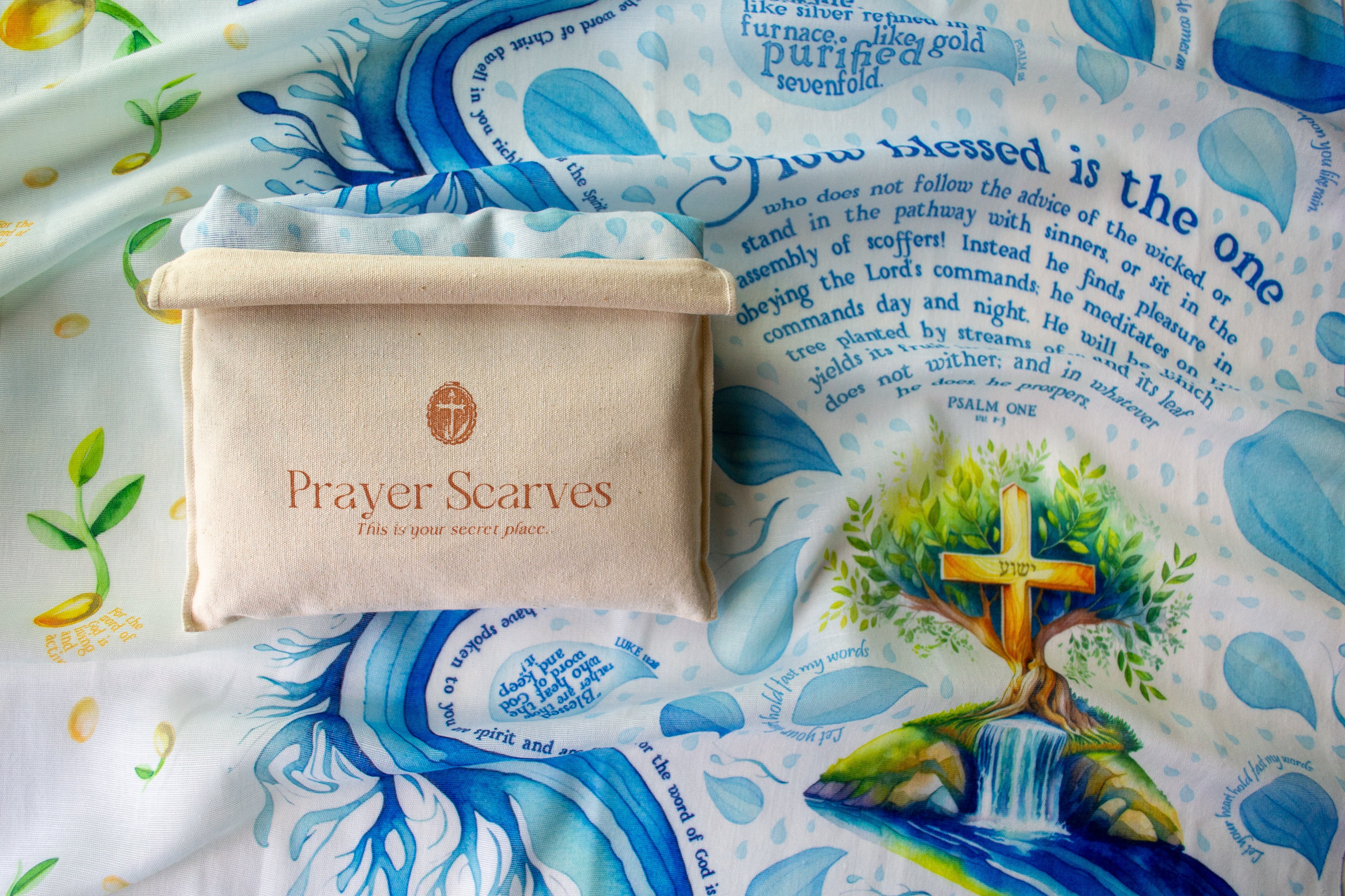 Seed of Life prayer scarf by Prayer Scarves® shown in close detail, featuring blue water-inspired illustrations, raindrop motifs, a tree with a cross at its center, visible Psalm scripture text next to a canvas bag