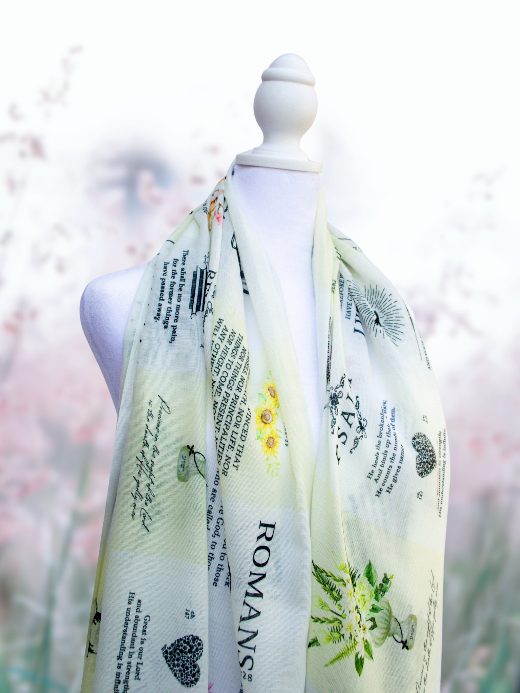 Dawn prayer scarf by Prayer Scarves® shown draped over a white mannequin, featuring a light ivory background with botanical illustrations, visible scripture text including Romans, Psalm references, floral motifs, and decorative typography throughout the design.