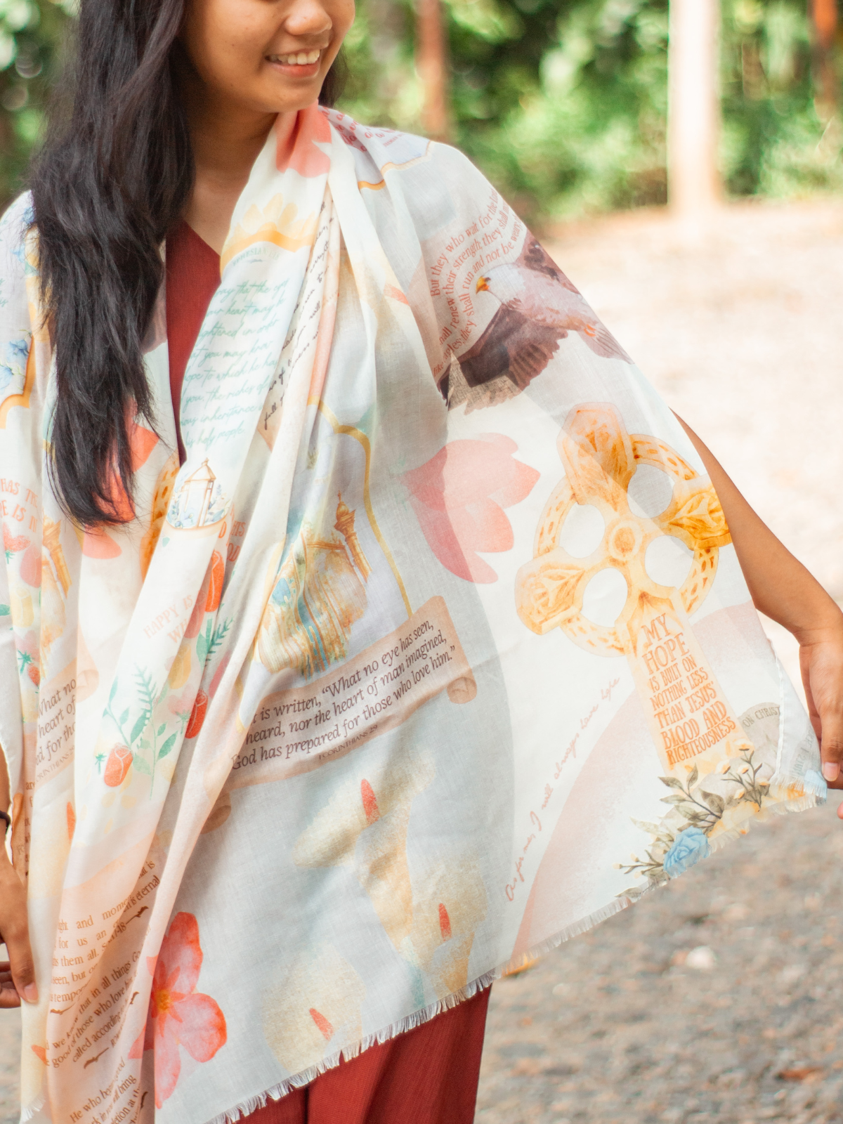 Hope prayer scarf by Prayer Scarves® worn outdoors in the honeysuckle colorway, featuring soft peach, yellow, and blue floral elements, framed scripture text panels, handwritten-style typography, and illustrated motifs visible across the fabric.
