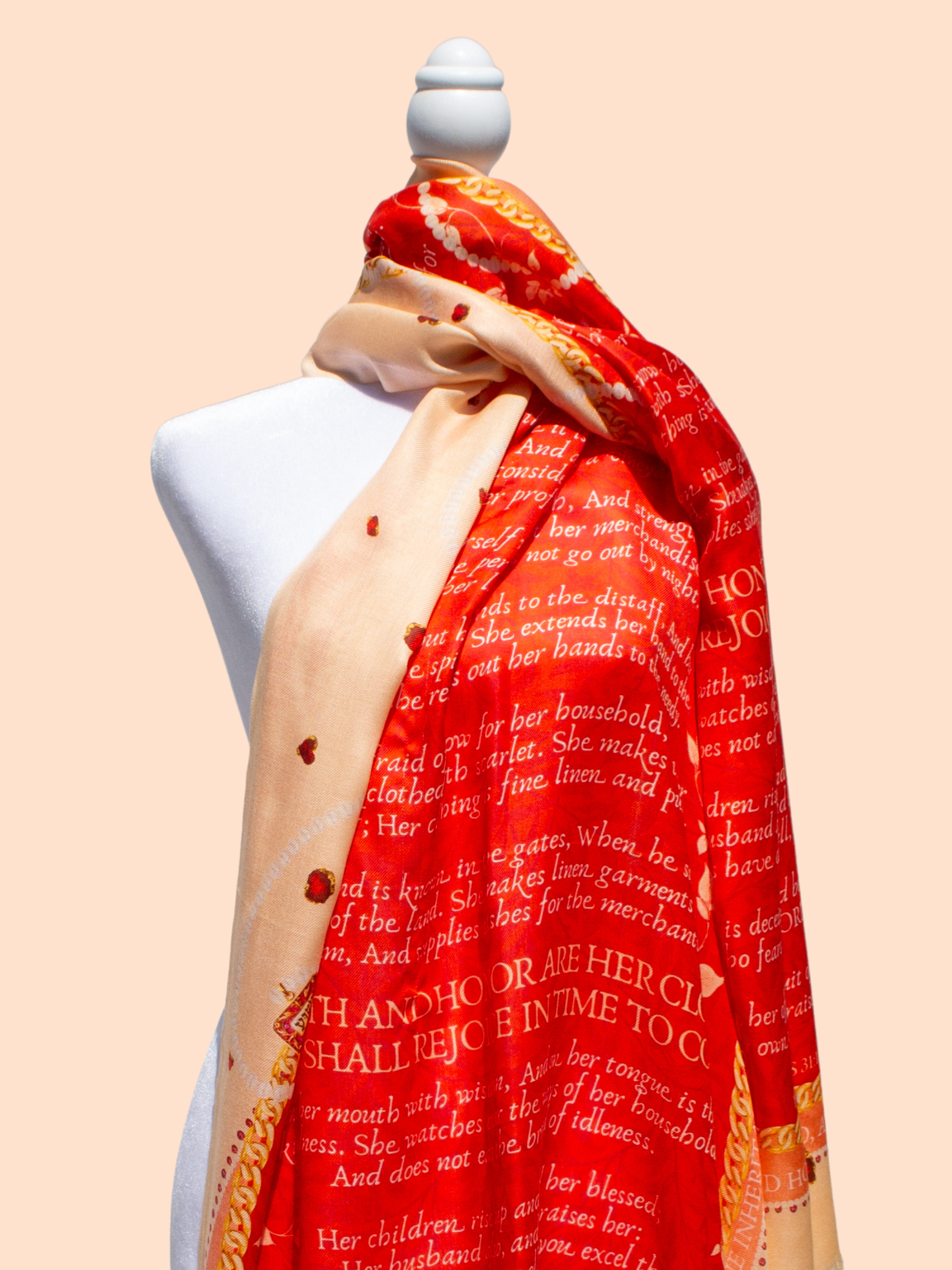 Prayer Scarves® Proverbs 31 Virtuous Woman scarf in orange and warm peach tones displayed on a mannequin, featuring Proverbs 31:10–31 scripture text across the fabric, floral vine accents, jewel-like motifs, and gold-toned ornamental border details.