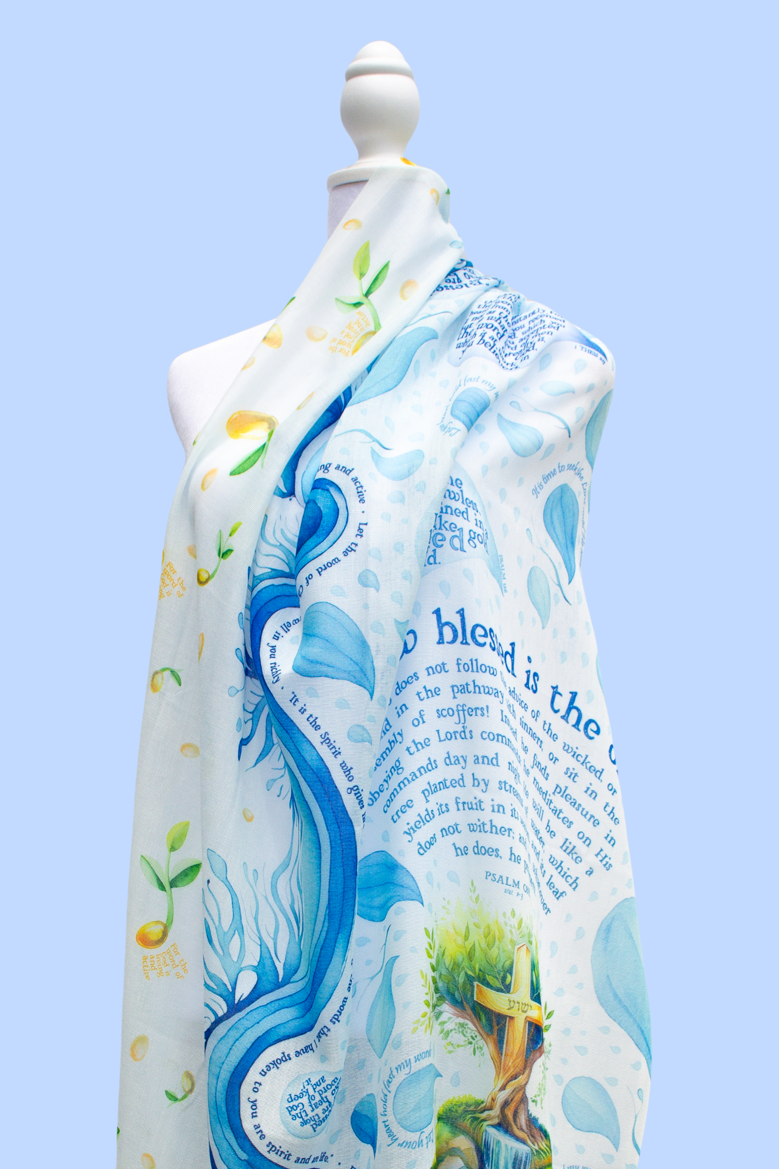 Seed of Life prayer scarf by Prayer Scarves® displayed on a mannequin, featuring flowing blue and white water-inspired illustrations, leafy green accents, a tree motif, and visible Psalm scripture text integrated throughout the design.