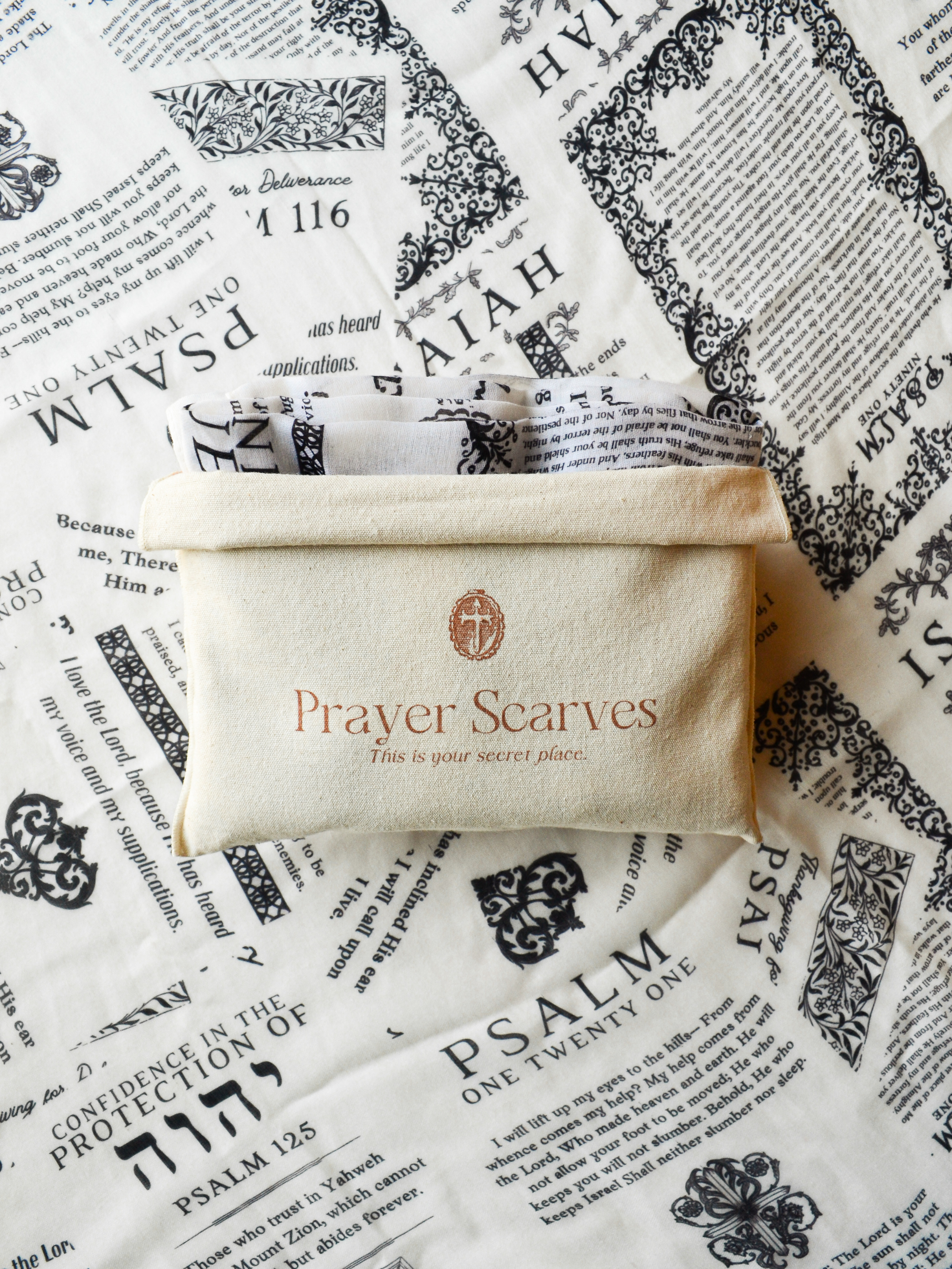 Protection prayer scarf by Prayer Scarves® shown with branded fabric pouch, laid over Scripture-printed scarf featuring passages about God’s protection from Psalms and Isaiah