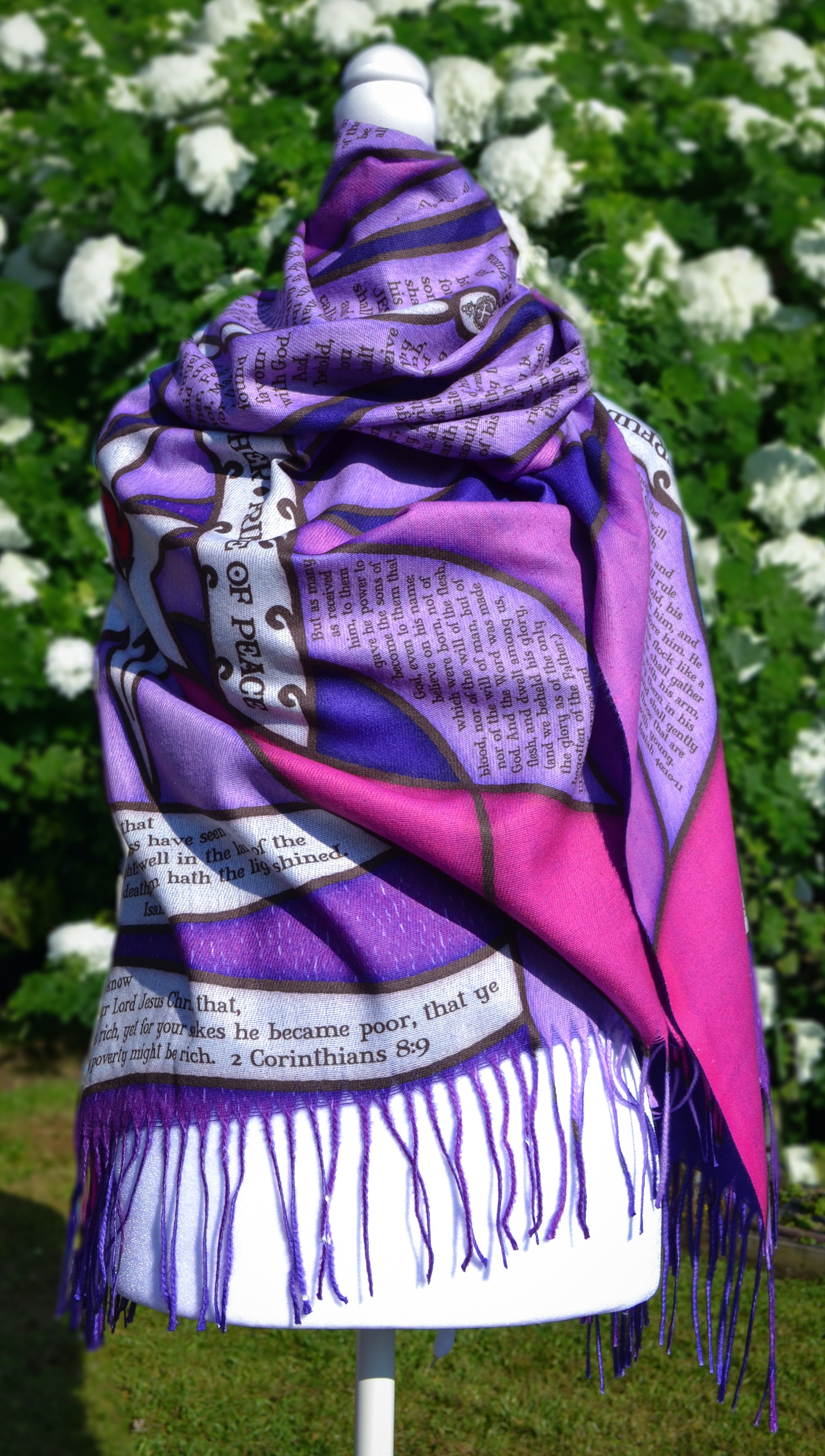 Purple Advent Prayer Scarf by Prayer Scarves® shown draped on a mannequin outdoors, highlighting stained-glass–style purple and pink sections, black lead-style lines, a central flame design, and printed scripture elements.