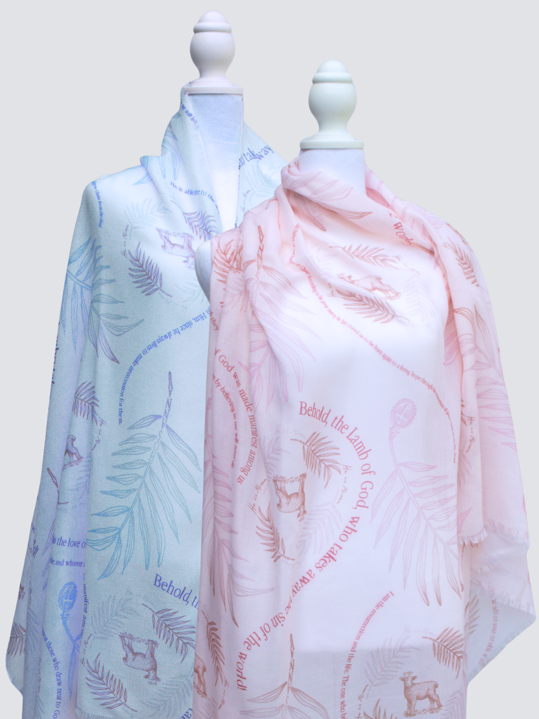 Hosanna prayer scarf by Prayer Scarves®, displayed on two mannequins in soft blue and blush colorways, featuring palm branches, lamb imagery, and scripture-inspired Hosanna text throughout the design