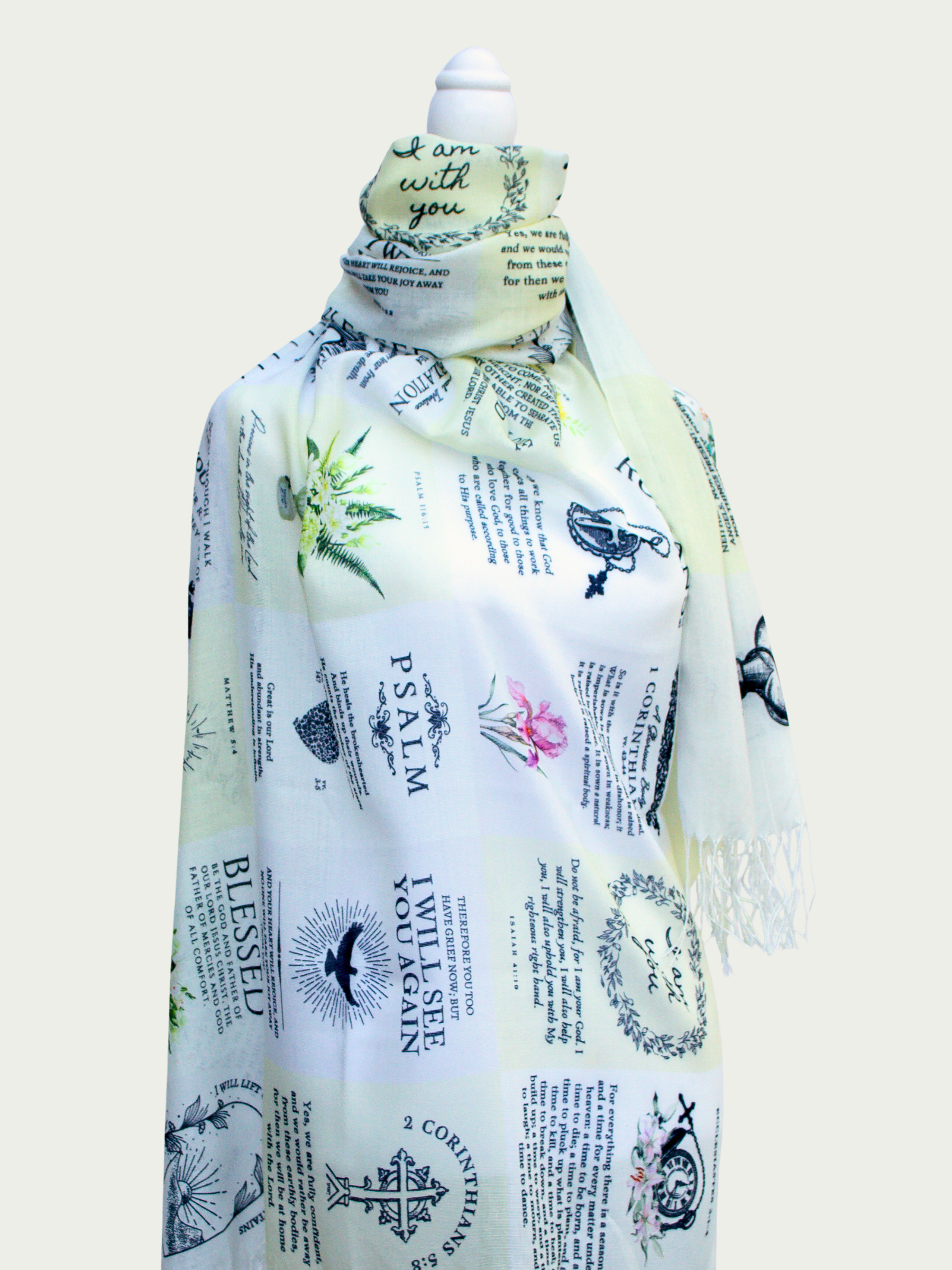Dawn prayer scarf by Prayer Scarves® shown draped over a white mannequin, featuring a light ivory background with botanical illustrations, visible scripture text including Romans, Psalm references, floral motifs, and decorative typography throughout the design.