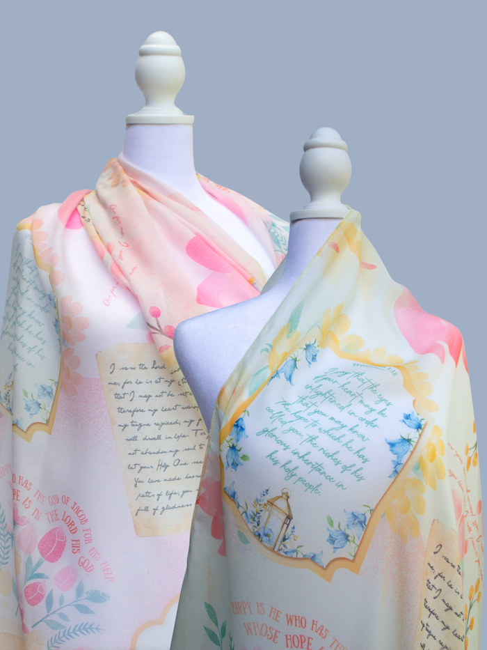 Hope prayer scarf by Prayer Scarves® displayed on two white mannequins, showing the Hope scarf in honeysuckle and pink colorways, with soft pastel florals, framed scripture text panels, handwritten-style typography