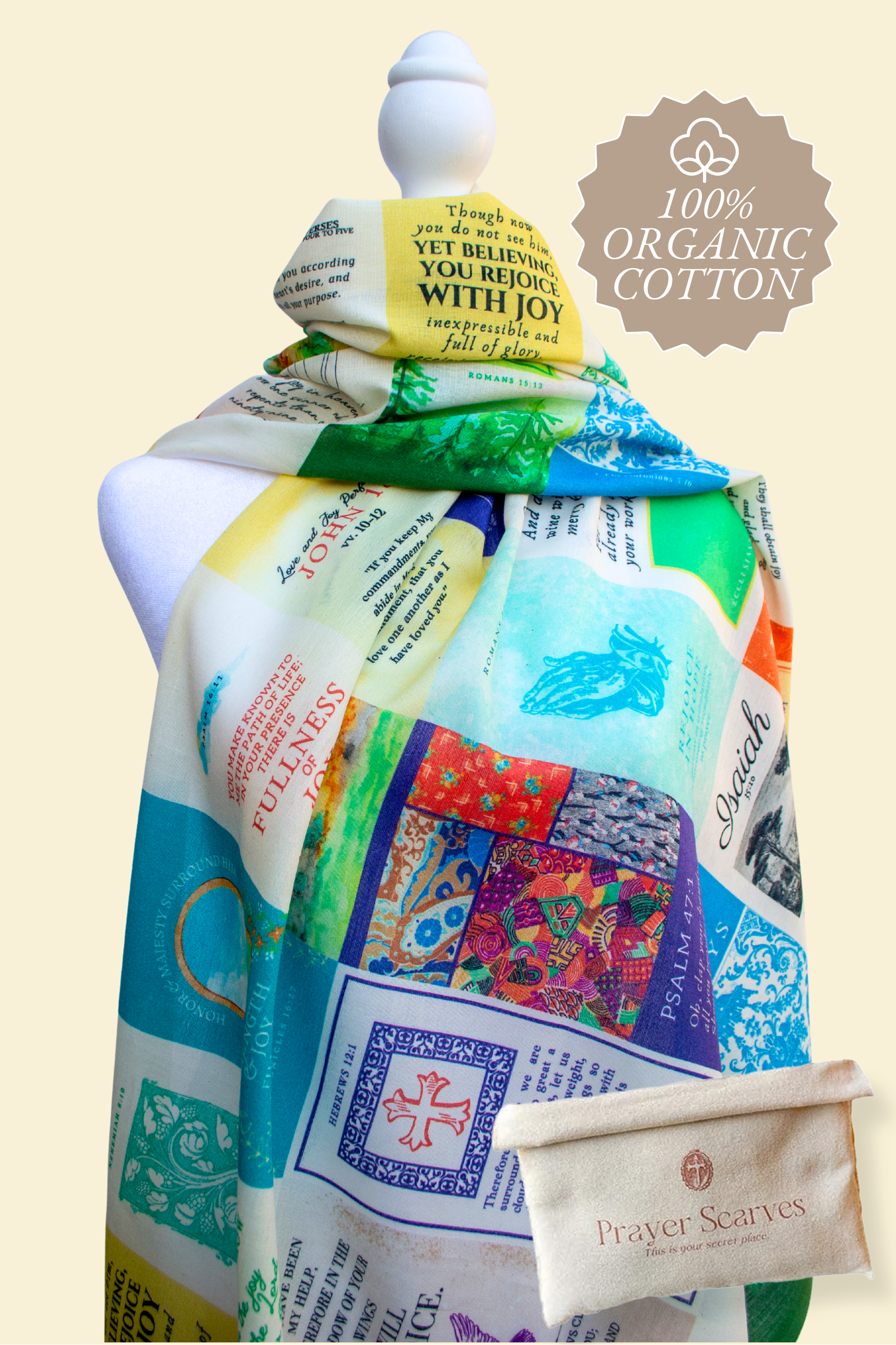 Joy Cotton prayer scarf by Prayer Scarves® displayed on a white mannequin, featuring a multicolor patchwork-style design with scripture text blocks, decorative patterns, and visible phrases including “Yet believing you rejoice with joy,” shown alongside a fabric storage pouch and a visible “100% Organic Cotton” badge.